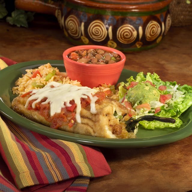 a plate topped with a bowl filled with beans, sided by a guacamole salad and a taco